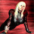 Pixelated image of a person with long blonde hair in a black outfit against a red background, seated with legs extended.