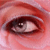 A close-up of a human eye with reddish-brown tones, showing detailed eyelid and iris textures in pixelated form.