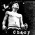 Pixelated grayscale image of a shirtless figure with a smooth head, standing against a dark background with scattered light pixels and partial text below.