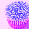 A cupcake with pink wrapper and blue sprinkles on a light purple background.