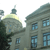Pixelated static image of a building with a domed roof and multiple windows, featuring muted green and blue tones against a light background.