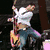 Animated sequence showing a person in various poses: playing guitar, standing with arms crossed, and holding a microphone, with background changes from dark to blue to red.
