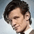 six shows a person with dark tousled hair and light skin, wearing a white-collared shirt against a pale blue background