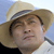 A pixelated close-up of a person wearing a light brown straw hat with a dark band, set against a light blue background.