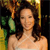 A pixelated image of a person with long dark hair wearing a strapless top, set against a blurred background with green and yellow tones.