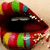Pixelated close-up of stylized lips with glossy red surface, black interior mouth cavity, and multicolored pixel clusters in yellow, green, blue, pink on upper and lower edges.
