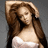 A woman with long brown hair in a white strapless top, one hand raised to her head against a gray background.