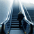 Pixelated image of a dark figure seated on a bench with vertical railings, set against a blue-toned background with light streaks.