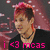 Pixelated image of a person with light skin and short brown hair, wearing a black top, with pink text reading 'i <3 mcas' at the bottom against a dark background with pink and white speckles.