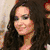 A woman with long dark hair appears in multiple views: smiling in profile, wearing a red top with a white cross pendant, and with a colorful rainbow background.