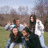 Group of people posing outdoors with trees and grass background, some wearing white jackets.