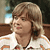 Pixelated image of a person with light brown hair wearing a white shirt with orange and brown patterns, set against a blurred background with brown and blue tones.