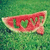A pixelated watermelon slice with red flesh and green rind on a green background, featuring a heart-shaped cutout in the center.