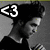 Pixelated grayscale image of a person wearing a black hat with white '<3' symbol on left side, viewed from side with head turned right.