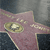 A pink star-shaped icon with a golden circular emblem and scattered light dots on a dark background.