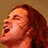 Pixelated close-up of a person with long brown hair looking upward, mouth open in an expressive pose against a solid brown background.