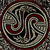 A circular icon with a swirling pattern of dark red, black, and muted gray tones forming a maze-like design within a rounded square frame.