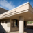 Pixelated image of a building with a sloped roof, columns, and windows under a blue sky with clouds.