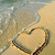 A pixelated beach scene with a heart-shaped sand drawing, gentle waves lapping at the shore under soft lighting.