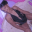 Pixelated image of a person in dark clothing holding an object against a purple and pink background.