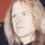 Pixelated close-up of a person with light-colored hair against a red and dark background, showing partial facial features and clothing.