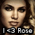 Pixelated close-up of a person's face with long dark hair, wearing light-colored clothing and displaying a neutral expression beneath text reading 'I <3 Rose' in blocky white letters on black background.