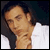 Static pixelated image of a person's face and upper neck in profile view with dark hair, light skin tone, and white clothing against a dark background.