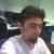 Pixelated static image of a person wearing dark cap and white shirt against blurred green background.