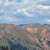Pixelated landscape with blue sky and scattered clouds above a brownish terrain with green patches.