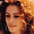 Pixelated close-up of a person with light brown hair tied back, wearing a dark top against a warm-toned background.