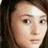 Pixelated close-up of a person's face with light skin tone, dark hair, and neutral expression against dark background.