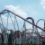 Pixelated image of a roller coaster track against a light blue sky with white clouds, showing multiple loops and twists in the structure.