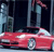 A red convertible car with a white roof is positioned in front of a dark building with tall windows and a blue-tinted facade.