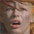 A pixelated close-up of a person's face with light skin, brown hair, and an open mouth showing teeth, set against a blurred background.