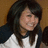 Pixelated image of a person with long dark hair wearing a white top with dark sleeves, set against a brown background.