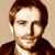 Pixelated static image of a person with brown hair and dark clothing against a light background, rendered in low-resolution style typical of early 2000s digital icons.