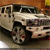 Pixelated static image of a light-colored vehicle with dark wheels and windows, positioned on a textured surface under warm lighting.