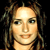 Pixelated close-up of a person with light skin tone, brown curly hair, and a neutral expression against a black background.