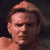 Pixelated static image of a person's face with light brown hair and visible facial features against a dark background.