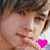 A person with brown hair and light skin holds a hand near their mouth, wearing a pink heart symbol on the right side of the image.