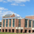 A static pixelated image of a multi-story building with columns under a blue sky with scattered clouds.