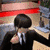 Animated sequence of a person in black suit and white tie playing drums with green drum kit, red background elements visible.