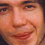 Pixelated close-up of a smiling person's face with visible eyes, nose, mouth, and skin tones in warm orange and brown hues.