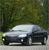 Static image of a silver sedan with dark accents parked on a light gray surface against a blurred green background.