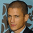 Pixelated close-up of a person with short brown hair, light skin, and a dark suit against a light blue background with blurred dark shapes.