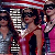 Pixelated static image of multiple people in a group pose with one central figure wearing red, surrounded by others in darker and lighter clothing against a dark background.