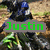 A pixelated image of a person in dark clothing and blue helmet riding a motorcycle on dirt terrain, with green text overlays.