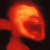 A pixelated image of a figure with an oversized head and mouth, standing before a group of people holding microphones under warm lighting.