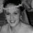 Static grayscale image of a person with short hair, closed eyes, and a wide smile, wearing a light-colored top against a dark background.