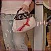A person holds a light-colored handbag with red stripes and a dark patterned section, wearing light blue jeans and a white top.